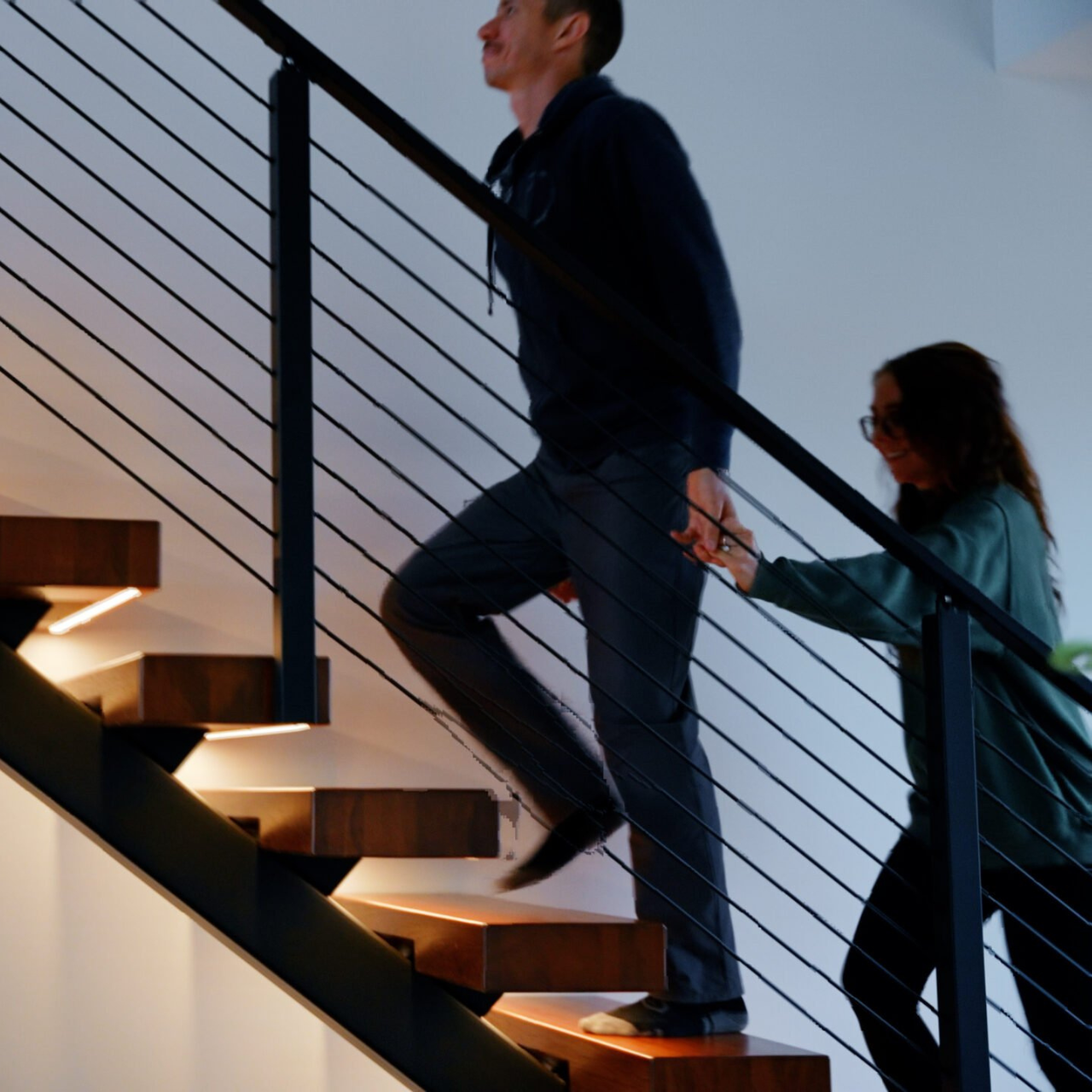 A man and a woman walk up a Viewrail FLIGHT Mono Staircase with LED lights underneath the treads.